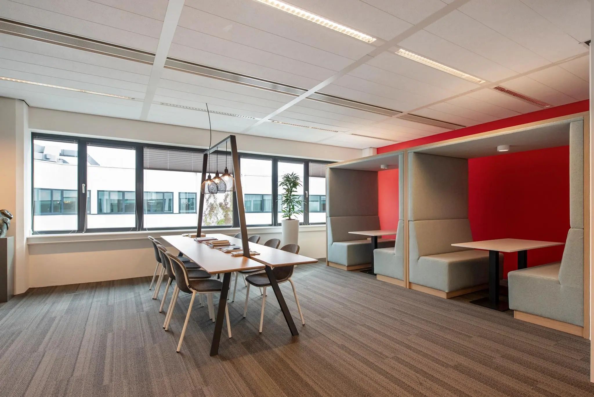 Moderne kantoorruimte aan de Grote Marktstraat met een vergadertafel, hanglampen en zitnissen tegen een rode accentmuur.